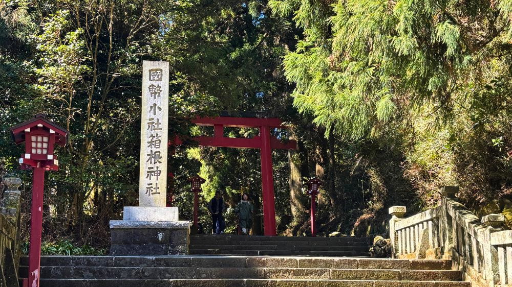 大きい石碑と赤い色の鳥居の舌を2人の男女がくぐっている。