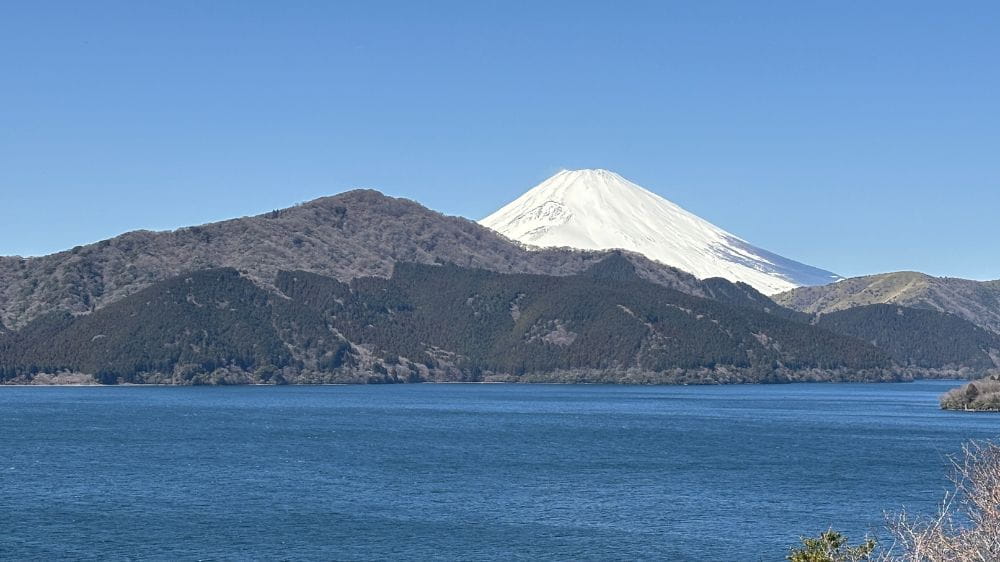 雪の覆われた山と、緑色の山が並ぶ。前に湖。
