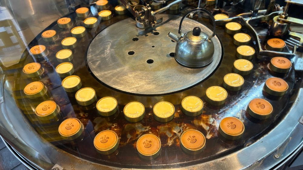 箱根湯本の老舗まんじゅう店で、焼きたての温泉まんじゅうが並ぶ調理機械の様子。