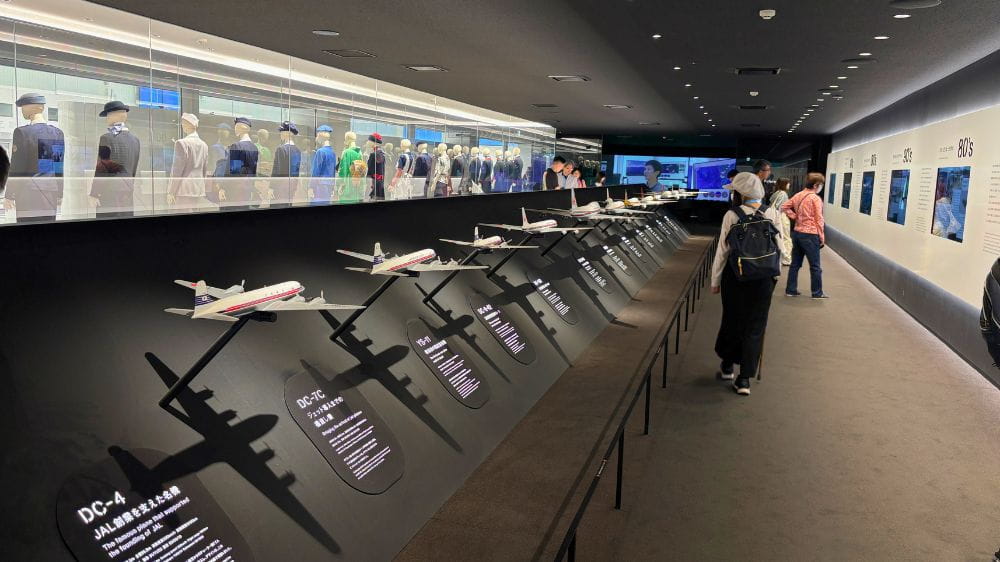 JALスカイミュージアムの展示エリアで航空機模型と歴代制服が並ぶ様子。