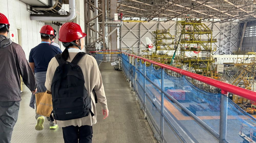 JALスカイミュージアムの見学で赤いヘルメットを着用し、整備工場内を見学する来場者の様子。