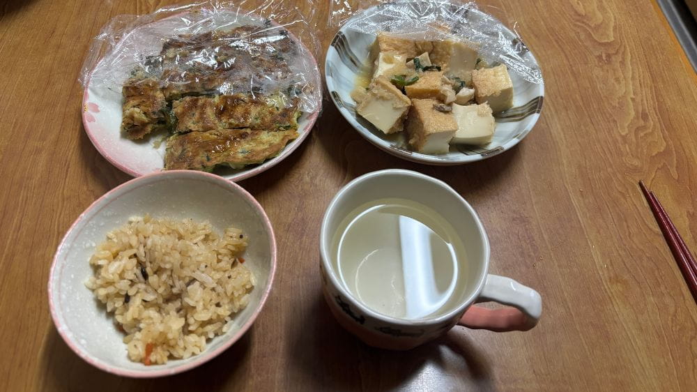 炊き込みご飯とおかず、温かい飲み物を並べたシンプルな食事の様子。