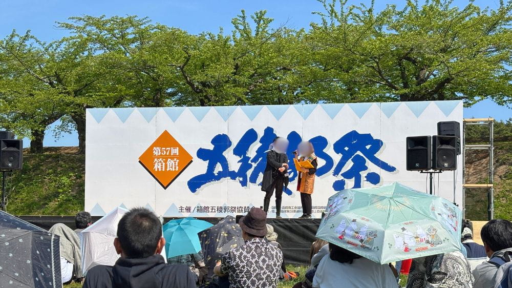 箱館五稜郭祭のステージイベントで司会者が進行する様子を観覧する来場者たち