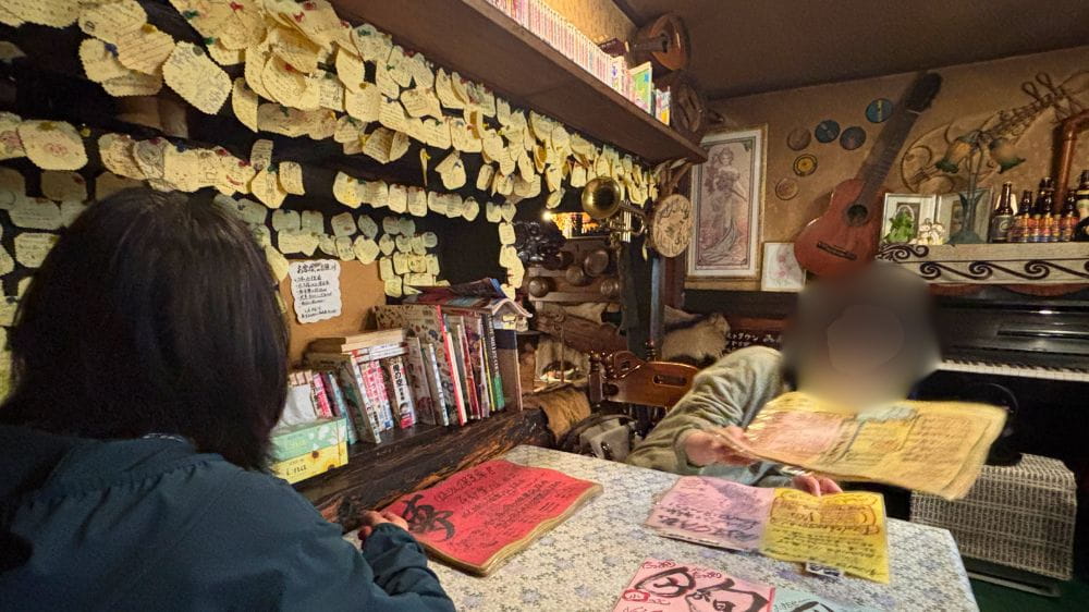 喫茶のんのんのレトロな店内で、店主から名物メニューの説明を受ける様子