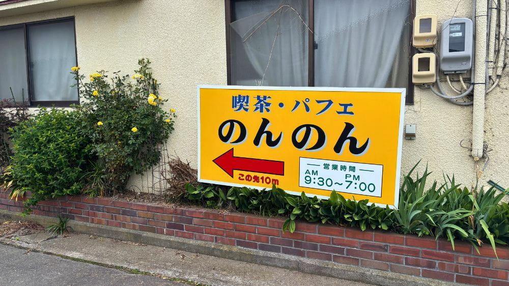 喫茶・パフェ「のんのん」の案内看板。営業時間(9:30~19:00)と店舗まで10mを示す矢印が設置されている。