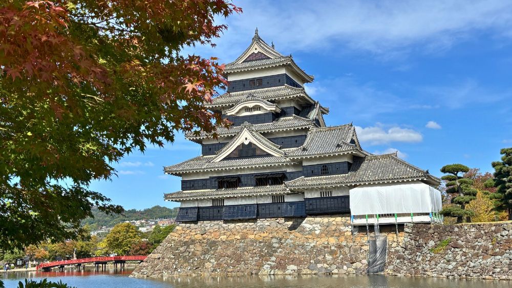 松本城公園から紅葉し始めた木々越しに眺めた松本城天守と石垣、水堀の景色
