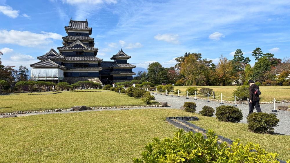 松本城の本丸御殿跡付近から眺めた天守と、芝生や植木が広がる本丸庭園