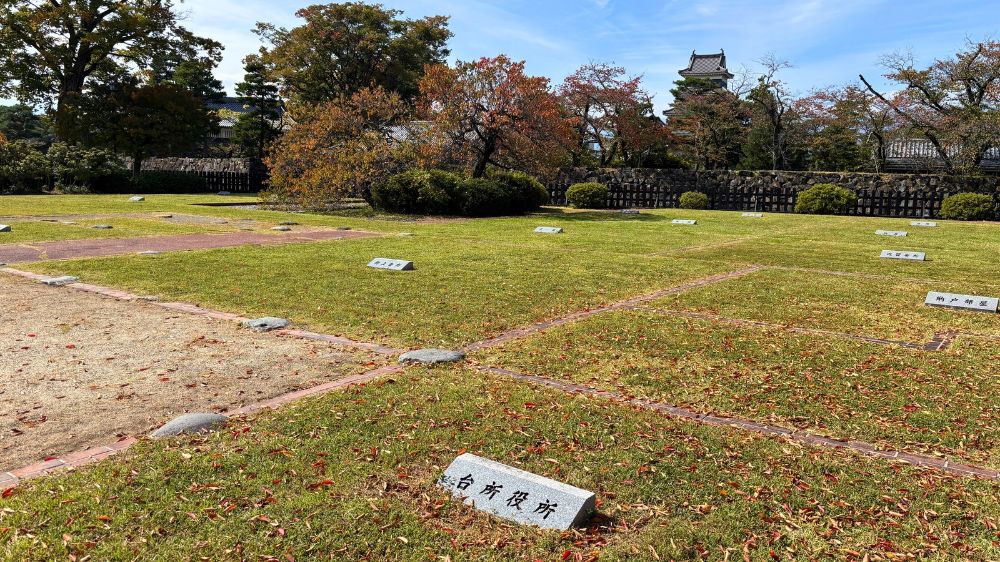 松本城の二の丸御殿跡に再現された部屋の区画と、芝生の上に設置された部屋名の案内表示