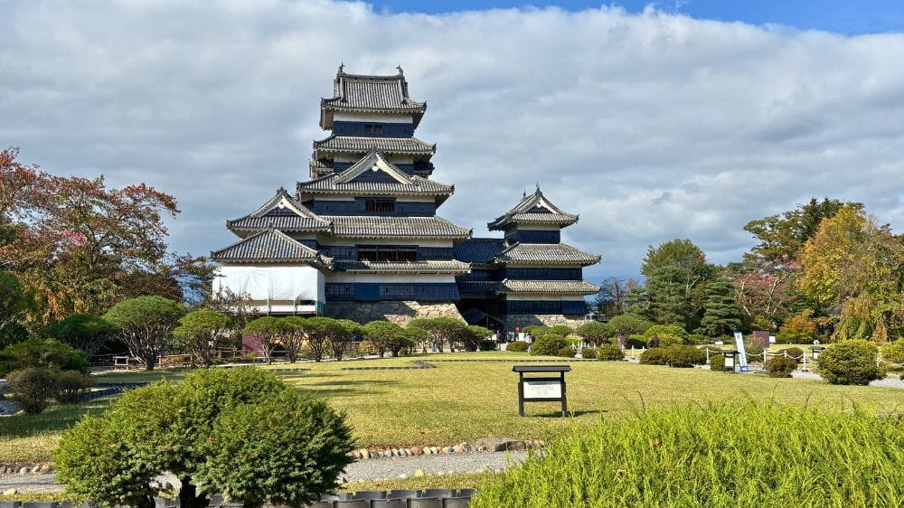 松本城の本丸庭園から撮影した天守の外観。手前には芝生と植木が広がる
